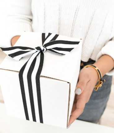 A person holding a beautifully wrapped gift box with an elegant black and white striped ribbon.
