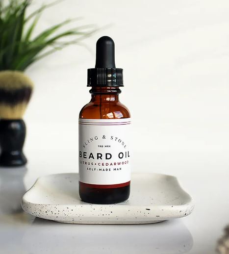 A bottle of beard oil placed on a ceramic tray with grooming accessories in the background, suggesting a men's grooming routine.