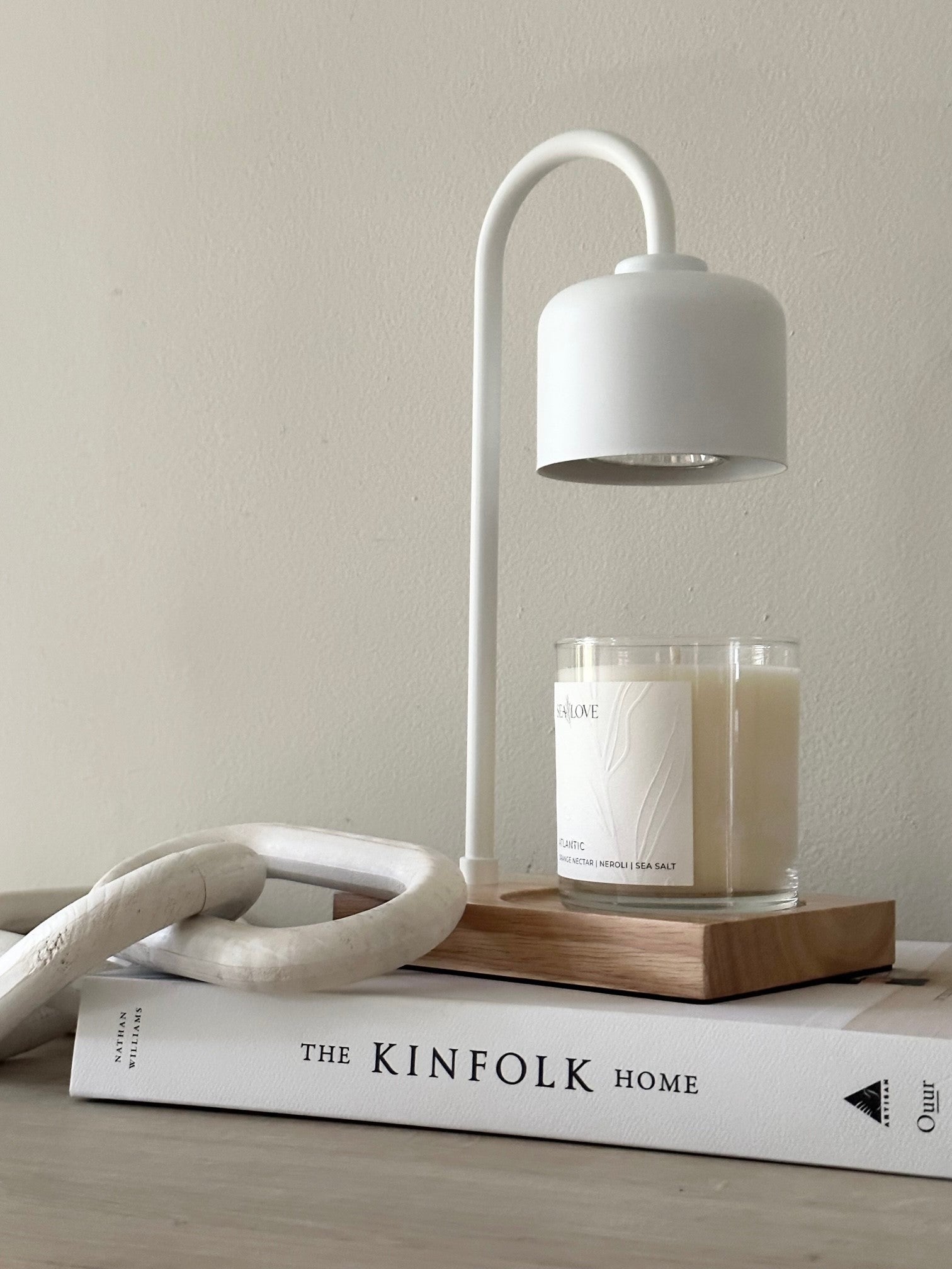 A serene and stylish corner featuring a modern white desk lamp perched atop a stack of design books, with a decorative knot sculpture and a lit scented candle providing a cozy ambiance.